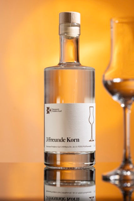 Der Drei-Freunde-Korn der Brennerei Karl abgebildet mit einem Glas und vor einem Orangenem Hintergrund.